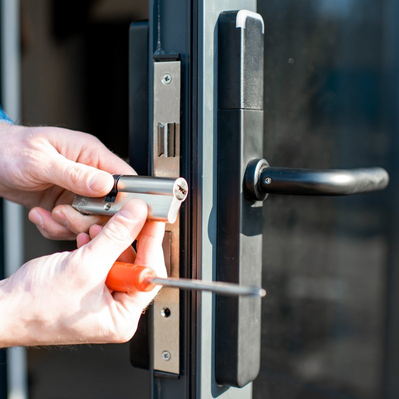 Cylinder lock barrel in a pair of man's hands with screwdriver, preparing to change on door